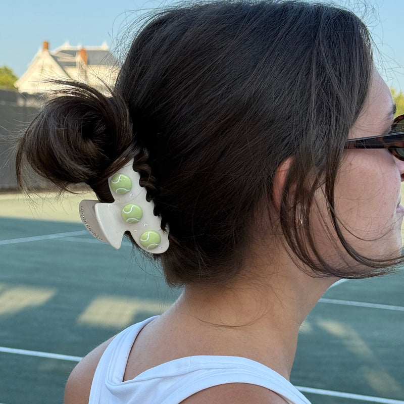 Person with hair tied back using a decorative hair tie on a tennis court